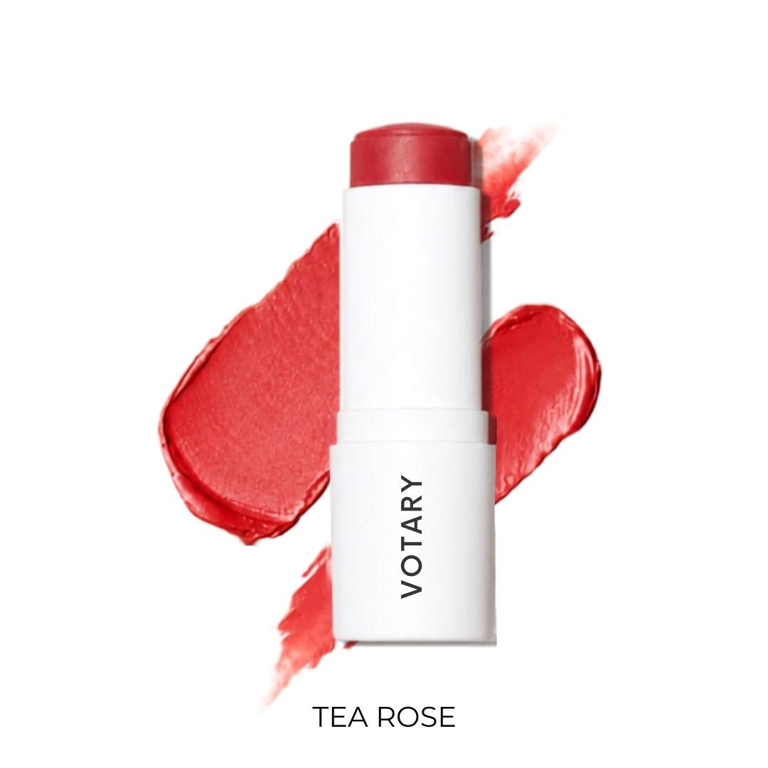 VOTARY Lip and Cheek Tint-TeaRose stick in a white tube with a red cap, shown in front of red cream makeup smears on a white background.