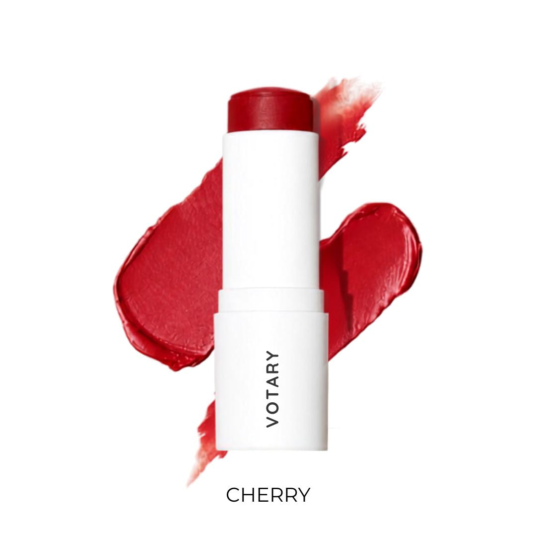 VOTARY Lip and Cheek Tint_Cherry stick in a white tube with a deep red cap, shown in front of red cream makeup smears on a white background.