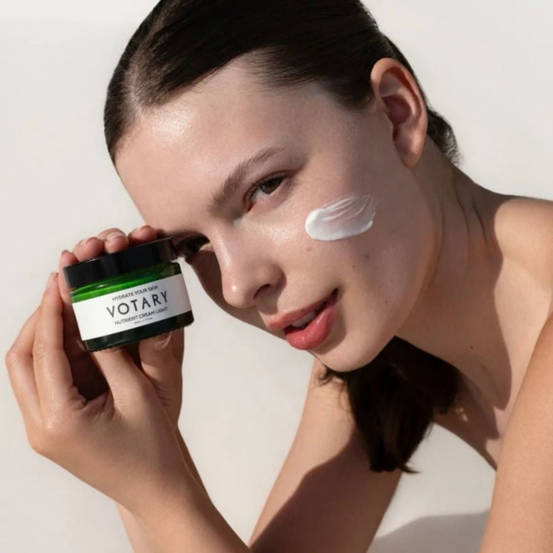 Woman holding Votary Nutrient Cream Light with moisturiser applied to her cheek