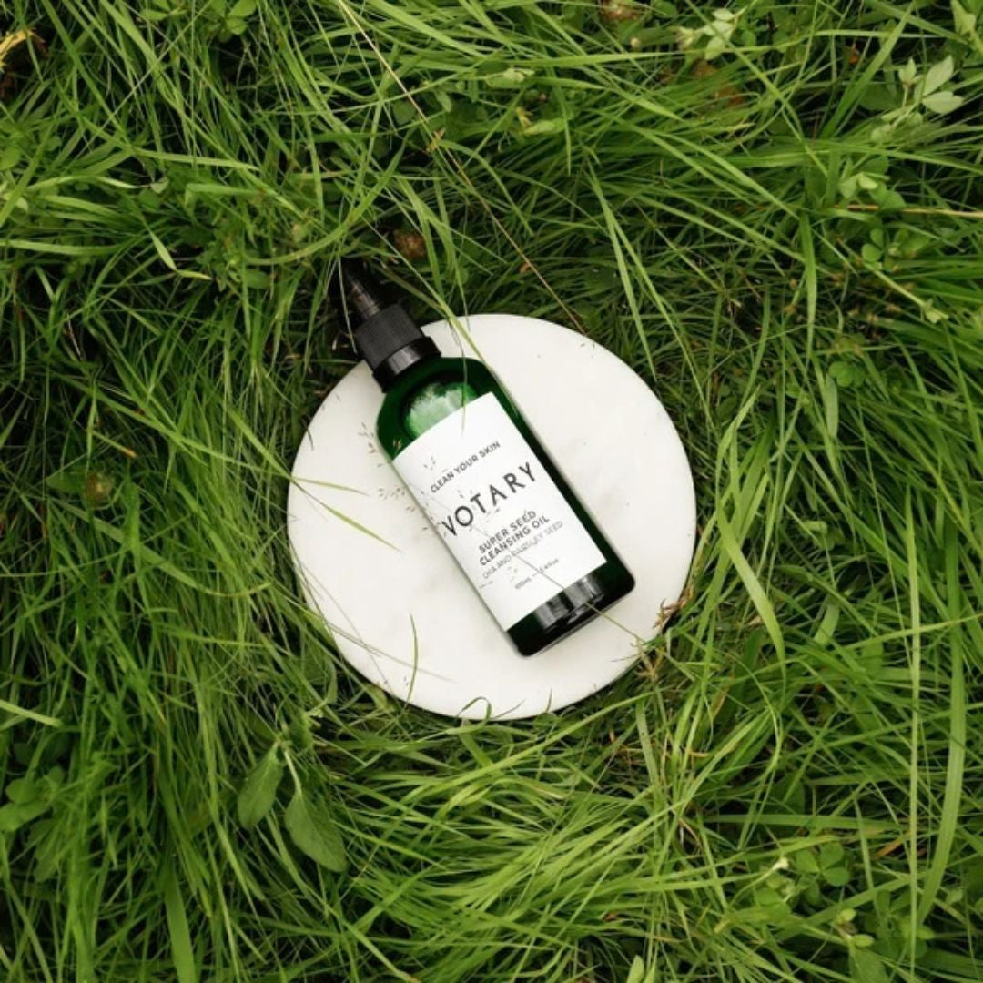 Votary Super Seed Cleansing Oil with chia and parsley seed in green bottle displayed outdoors on fresh grass