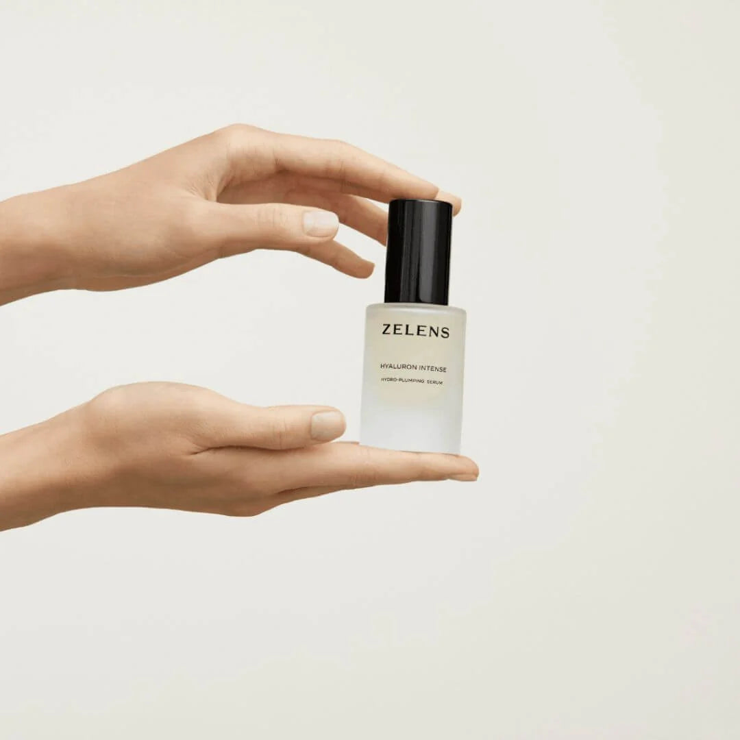 Zelens Hyaluron Intense Hydro-Plumping Serum 30ml – lifestyle shot: hands holding frosted glass serum bottle against off-white background