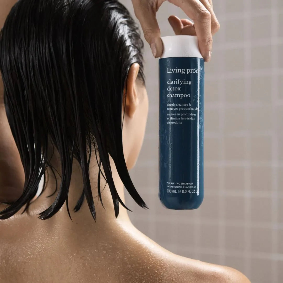 Person holding a bottle of Living Proof shampoo with wet hair