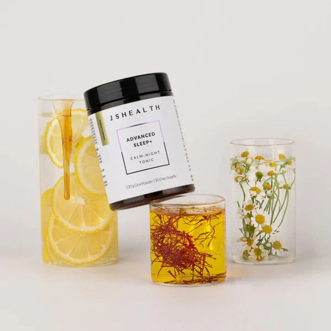 JSHealth Advanced Sleep+ Calm Night Tonic Powder 120g – lifestyle flat lay: powder jar with lemon slices and prepared glass of tonic on white background