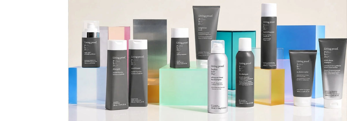 Living Proof Perfect hair Day product lineup including shampoo, conditioner, night cap overnight perfector, 5-in-1 styling treatment, weightless mask, advanced clean dry shampoo, dry shampoo, heat styling spray, in-shower styler, and triple detox shampoo, displayed on colored glass blocks.