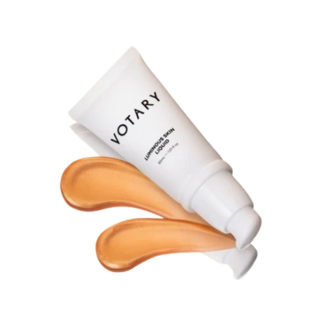A white squeeze tube of VOTARY Lumino Skin Liquid Cream with two swatches of the peach-colored cream product in front, on a solid white background.
