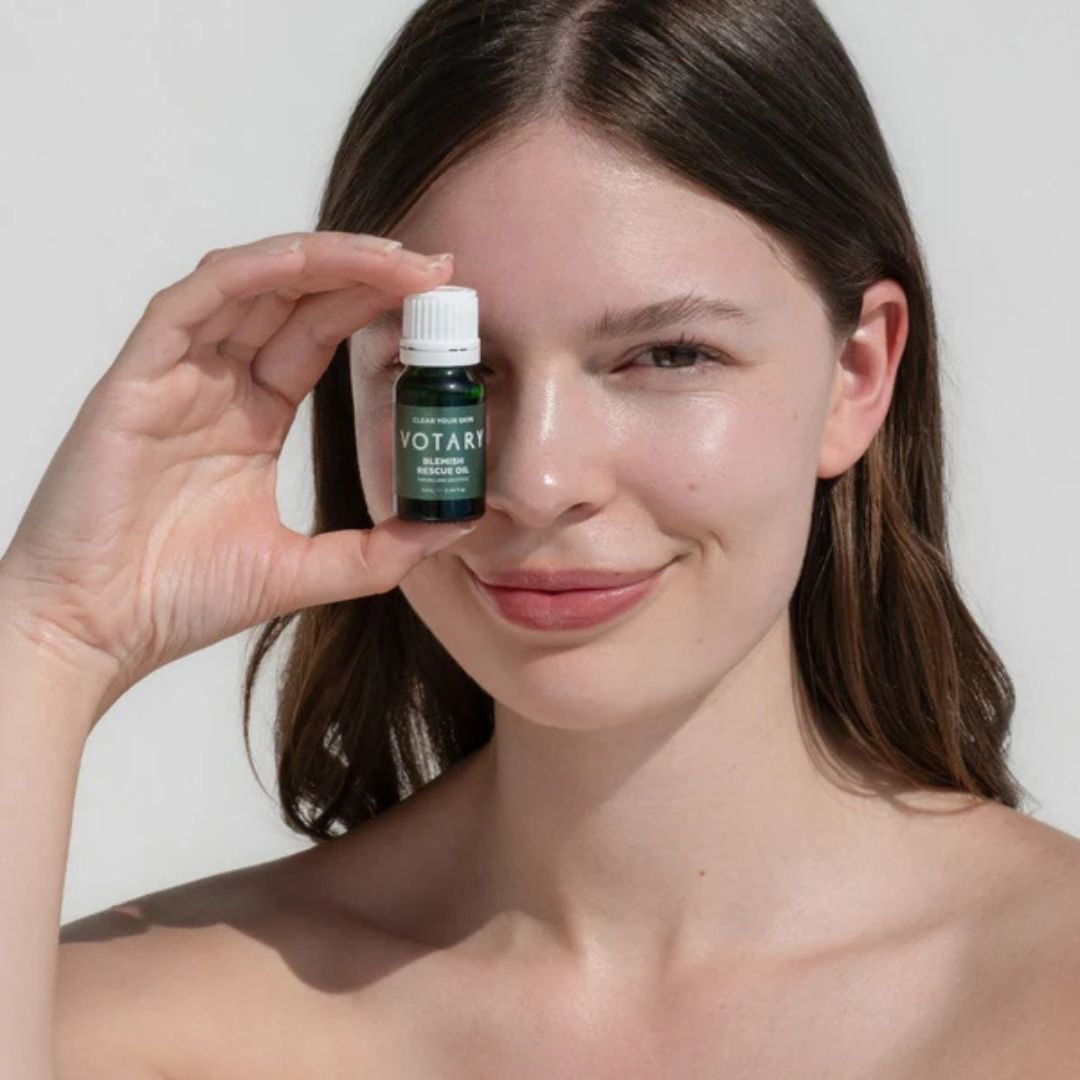 Woman holding Votary Blemish Rescue Oil with Tamanu and Salicylic beside her face