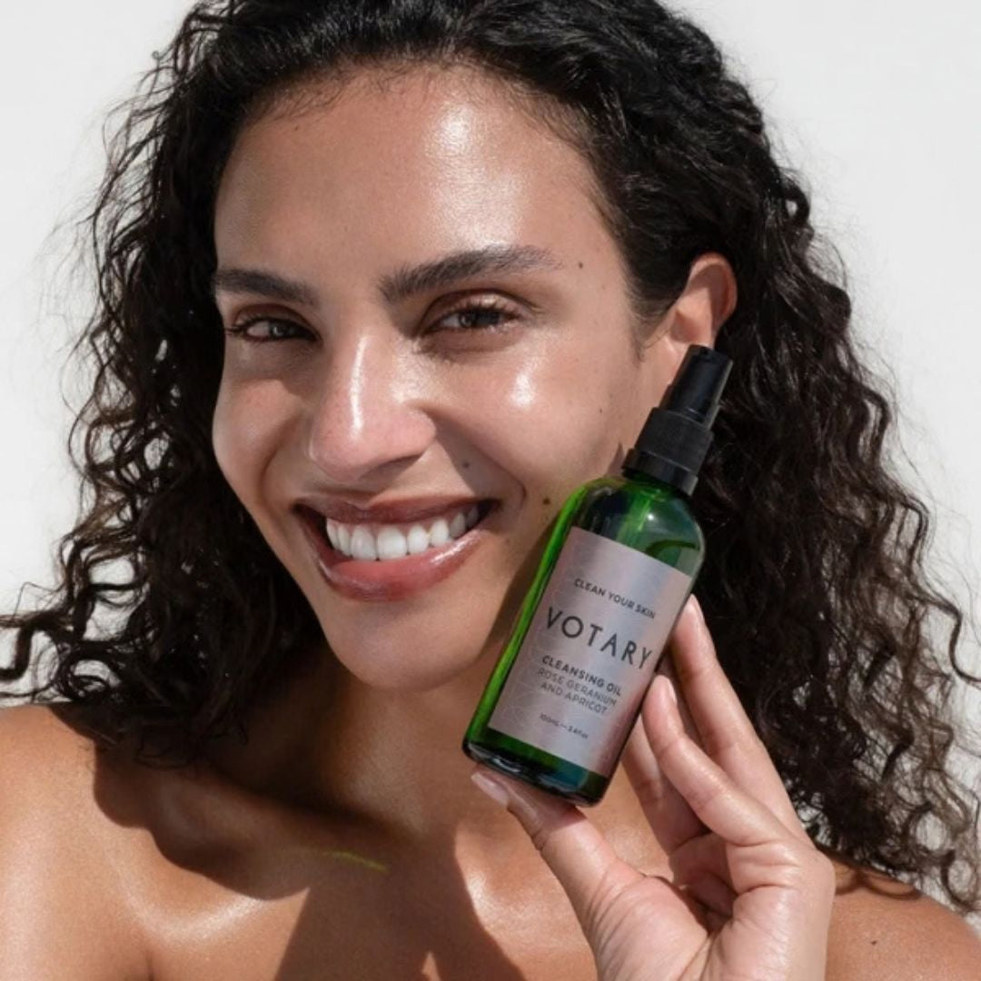 Votary Cleansing Oil Rose Geranium & Apricot held beside face, nourishing facial cleansing oil for removing makeup and cleansing skin