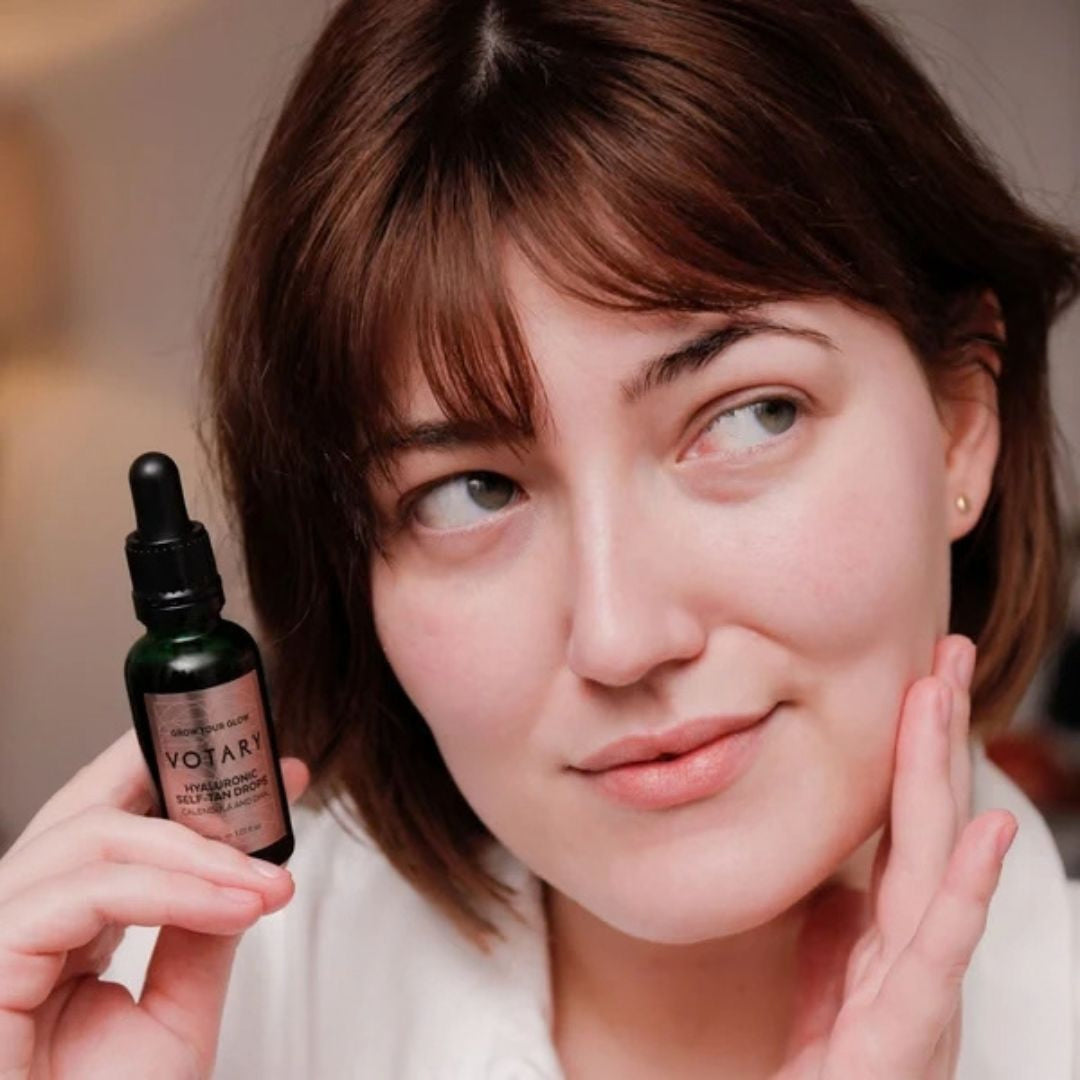 Woman holding Votary Hyaluronic Self-Tan Drops beside her face for a hydrated sun-kissed glow