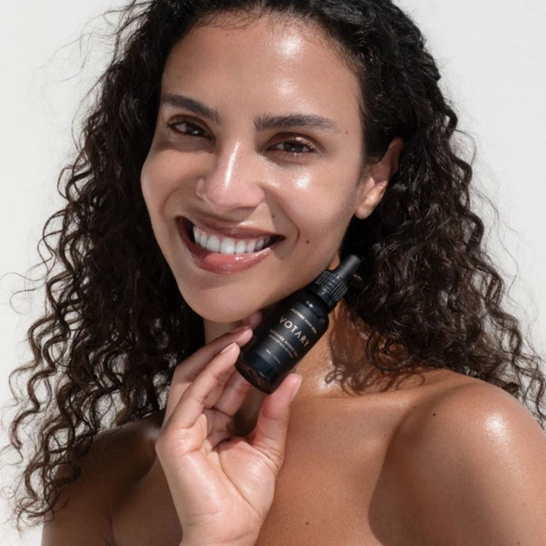 Woman holding Votary Intense Night Oil with Rosehip and Retinoid beside her face