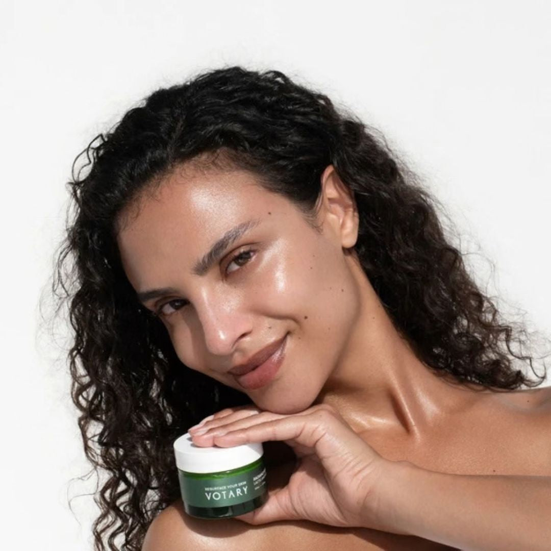 Woman holding Votary Radiance Reveal Mask skincare jar against a clean white background