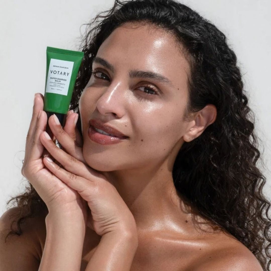 Woman holding Votary Super Barrier Balm with Cica and Probiotics beside her face