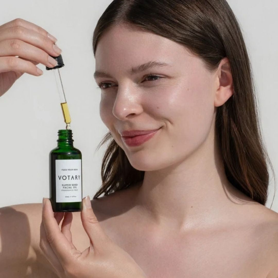 Woman holding Votary Super Seed Facial Oil with dropper above the fragrance-free face oil bottle