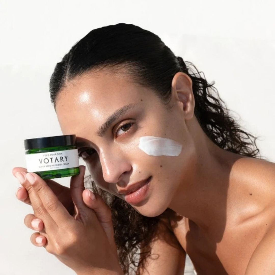 Woman holding Votary Super Seed Nutrient Cream with moisturiser applied to her cheek