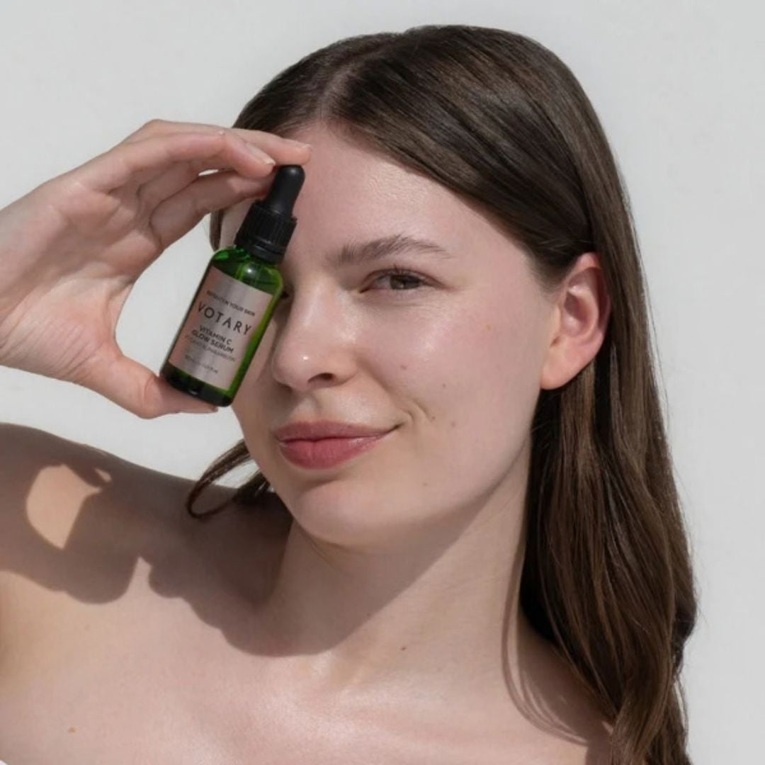 Woman holding Votary Vitamin C Glow Hyper-Pigmentation Serum with Niacinamide and Alpha Arbutin beside her face