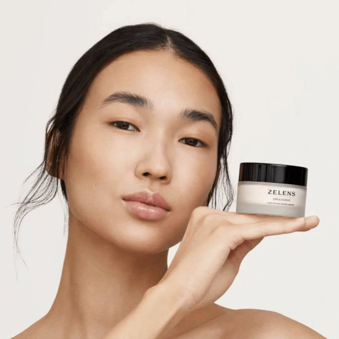 A woman holds a small white cosmetic jar with a black lid labeled ZELENS SMILE CARE against a clean light background.